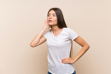 Pretty young girl over isolated background listening to something by putting hand on the ear