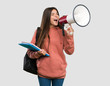 © luismolinero - Young student woman holding notebooks shouting through a megaphone over isolated grey background