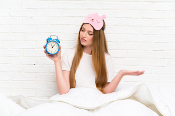 Young woman in dressing gown in bed holding vintage clock