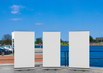 Wall Mural - 3D rendering of blank vertical rollup (empty billboard advertisement) with city background. Empty mockup template