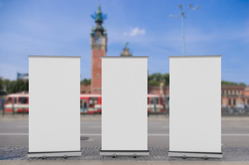 Wall Mural - 3D rendering of blank vertical rollup (empty billboard advertisement) with city background. Empty mockup template