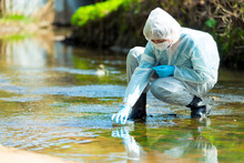 Scientist Researcher In Protective Suit Takes Water For Analysis From Polluted River
