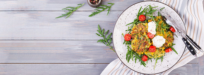 Zucchini pancakes with corn and sour cream served arugula, tomatoes salad. Banner. Top view