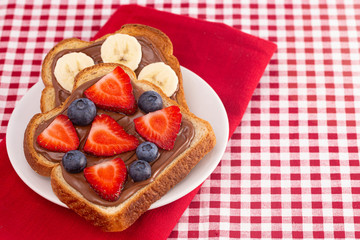 Pair of Fruit and Chocolate Hazelnet Spread Toast on a Red and White Plaid Tablecloth