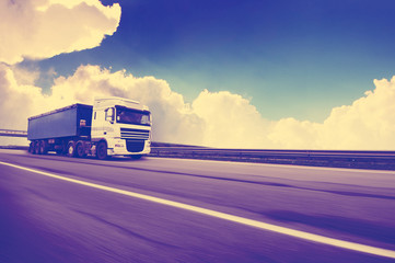 Wall Mural - Truck with a trailer in motion on the countryside road against sky with clouds and vintage color style