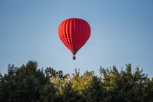 Red Hot Air Balloon In The Sky Above The Trees