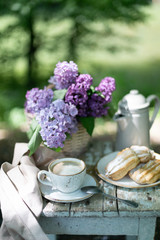 Wall Mural - Breakfast in the garden: eclairs, cup of coffee, coffee pot, lilac flowers in a basket.