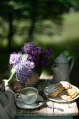 Wall Mural - Breakfast in the garden: eclairs, cup of coffee, coffee pot, lilac flowers in a basket.