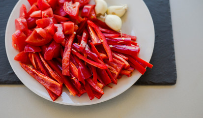 Wall Mural - Slices of fresh red hot chili peppers and tomatoes with garlic on white plate, close-up