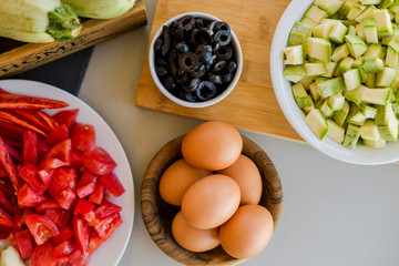 Wall Mural - Plates with sliced vegetables and eggs with olives in bowls on kitchen table, cooking process concept