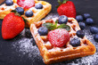 Homemade Traditional belgian waffles with fresh fruit, berries and sugar powder on black plate.