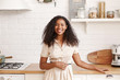 © Anatoliy Karlyuk - Food, cuisine, cookery and household concept. Beautiful cheerful young dark-skinned woman with Afro hairstyle standing at kitchen counter, making breakfast for her family, smiling broadly at camera