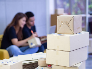 Wall Mural - Close-up of parcel boxes on the table with a woman and man sitting on a sofa with a blurred background