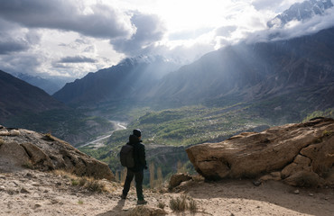 Wall Mural - a man with backpack standing on top of mountain with sunlight through cloudy sky. travel lifestyle a
