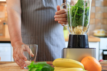 Elderly man is making fresh vitamin juice smoothie with spinach and banana