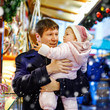 Middle aged father holding baby daughter near sweet stand with gingerbread and nuts. Happy family on Christmas market in Germany. Cute girl eating cookie called Lebkuchen. Celebration xmas holiday.