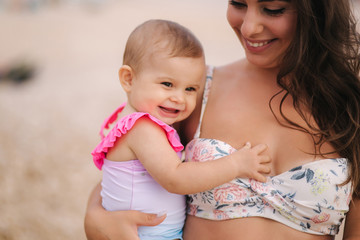 portrait of mother hold baby girl on hands on the beach in the sea. mom and daughter in swimsuit. cl