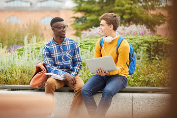 Portrait of two international students chatting while relaxing outdoors in college campus, copy space