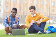 © Seventyfour - Full length portrait of two college students studying outdoors sitting on green lawn in campus, copy space