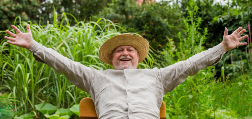 Wall Mural - An elderly man with a straw hat is happy and satisfied. He is sitting in a garden. Concept happy people.
