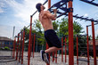 © zamuruev - Strong muscular man doing push-ups on uneven bars in outdoor street gym. Workout lifestyle concept.