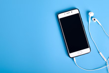  Mobile Headphones And A Mobile Phone Of White Color On A Blue Background In Light Colors With A Place For Text.
