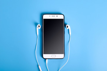  Mobile headphones and a mobile phone of white color on a blue background in light colors with a place for text.