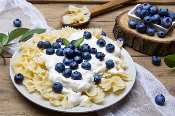 Wall Mural - Tasty pasta with fresh organic blueberries and vanilla cream. Sweet dinner on retro wooden table.