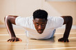 © twinsterphoto - Portrait of young African American man doing push-up on the floor. Determined male fit sportsman looking at camera