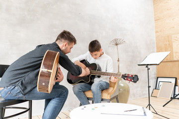 Two brother playing guitar. Older brother teaches younger one to play chords correctly