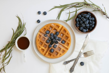 Wall Mural - Belgian Waffle with Blueberries and Maple Syrup, Dusted with Powdered Sugar, Flay Lay on White Background, Copy Space
