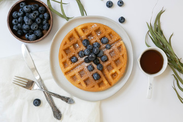 belgian waffle with blueberries and maple syrup, dusted with powdered sugar, flay lay on white backg
