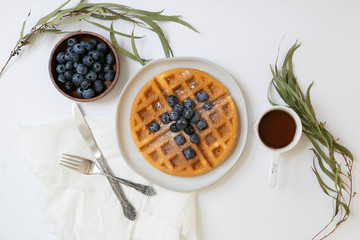 Wall Mural - Belgian Waffle with Blueberries and Maple Syrup, Dusted with Powdered Sugar, Flay Lay on White Background, Copy Space