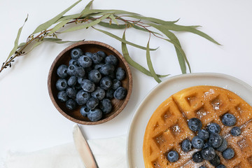Wall Mural - Belgian Waffle with Blueberries and Maple Syrup, Dusted with Powdered Sugar, Flay Lay on White Background, Copy Space