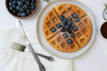 Wall Mural - Belgian Waffle with Blueberries and Maple Syrup, Dusted with Powdered Sugar, Flay Lay on White Background, Copy Space