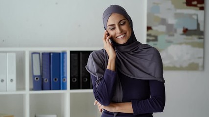 Wall Mural - Muslim woman received an anticipated call at the office. She's happy to talk with that person.