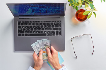 Male hands working on a laptop. Office workplace on a white table. Men's hands count American paper . The view from the top.