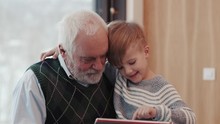 Smiling Grandfather And Grandson Using Digital Tablet For Surfing Internet And Playing Game Near The Fireplace At Home Grandpa Adult Grandchild Child Childhood Communication Computer
