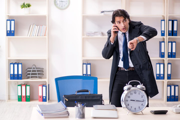 Young male employee in the office in time management concept