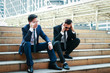 © SUPERMAO - Two businessmen sit at the public ladder. There is stress that is going to be unemployed.