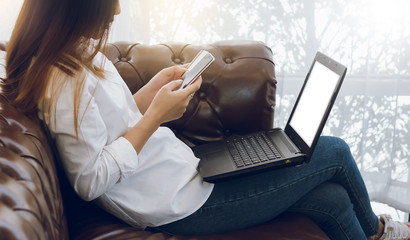 Wall Mural - Young asian woman sitting on sofa in living room she working with laptop and using credit card to payment and shopping on line with smartphone