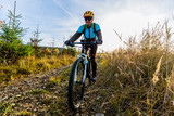 Fototapeta Lawenda - Mountain biking woman riding on bike in summer mountains forest landscape. Woman cycling MTB flow trail track. Outdoor sport activity.