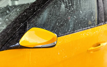 Front Side Mirror Of Bright Yellow Car Washed In Self Serve Carwash, Water Spraying Over Glass
