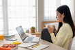 © weedezign - Asian female freelancer reading report on laptop and jot down note on table in bedroom at home.Work at home concept.work from home.relax lifestyle