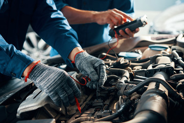 Close-up image of mechanic wearing protective gloves when using multimeter for testing automobile battery