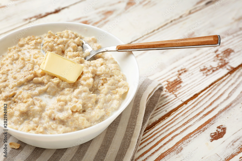Bowl with tasty oatmeal on white wooden table