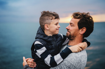 Wall Mural - Father with small son on a walk outdoors standing on beach at dusk.