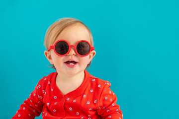 Wall Mural - Cute baby in red round sunglasses smile blue background