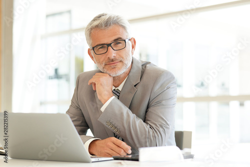 Fotomural Mature businessman sitting at desk looking at camera