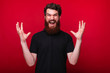 Young bearded man is screaming with raised hands on a red background.